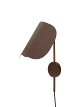 Angled view of the bronzed aluminium Wing Wall Lamp with its light on, highlighting the distinctive wing-shaped shade.